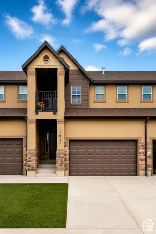 Multi-story exterior featuring stucco, stone accents, recessed balcony with metal railing, and attached multi-car garage