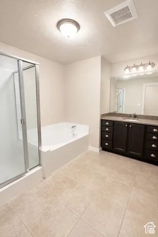 Primary Bathroom featuring a tiled shower with a glass enclosure, a deep soaking tub with a tiled surround, a dark wood-finish vanity with stone-style countertop, and tile flooring