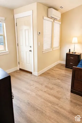Primary Bedroom: Vaulted ceiling featuring a central brushed-nickel ceiling fan, wall-mounted AC unit, with integrated lighting and wood-finish flooring. Access to Balcony.