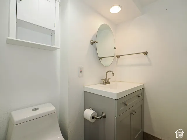 Grey vanity featuring a rectangular integrated sink, brushed-nickel hardware, oval wall-mounted mirror, and built-in upper cabinetry