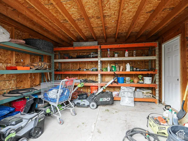 Storage structure featuring exposed wood-stud walls, open-joist ceiling, concrete flooring, and industrial-grade steel shelving units