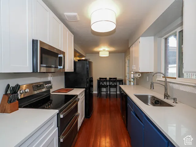 Kitchen featuring white and navy cabinetry, solid surface countertops, stainless steel appliances, and wood-finish flooring
