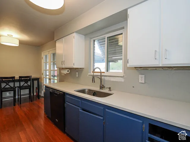 Kitchen featuring two-tone cabinetry, solid surface countertops, stainless steel undermount sink, brushed nickel pull-down faucet, and wood-finish flooring