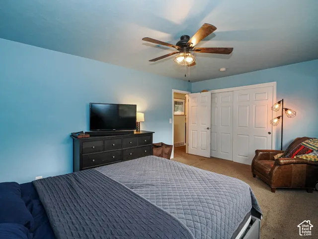 Room featuring a multi-blade ceiling fan with integrated lighting, wall-to-wall carpeting, and double-door closet cabinetry