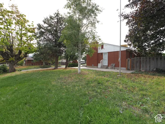 Red brick exterior featuring white horizontal siding, concrete patio, and mature trees situated on a grass lot with wood fencing