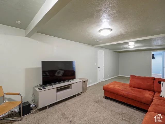 Expansive interior room featuring carpeted flooring, exposed ceiling beams, and flush-mount lighting
