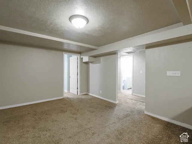 Neutral-toned interior space featuring wall-to-wall carpeting, crisp paint finishes, recessed structural beam detailing, a flush-mount ceiling fixture, and a six-panel door