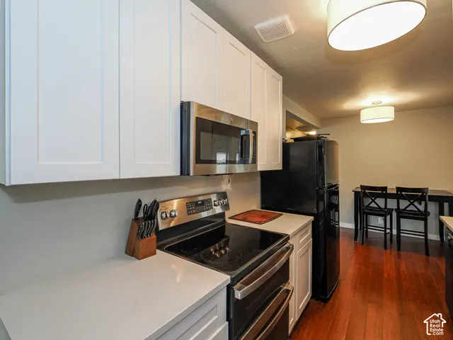 White shaker-style cabinetry, solid-surface countertops, stainless steel appliances, and wood-finish flooring