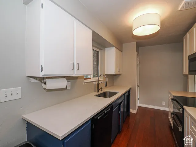 Kitchen featuring white upper cabinetry, blue lower cabinetry, solid-surface countertops, stainless steel sink with pull-down faucet, and wood-finish flooring
