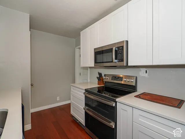 Kitchen featuring white shaker-style cabinetry, stainless steel oven, integrated microwave, solid-surface countertops, and wood-finish flooring
