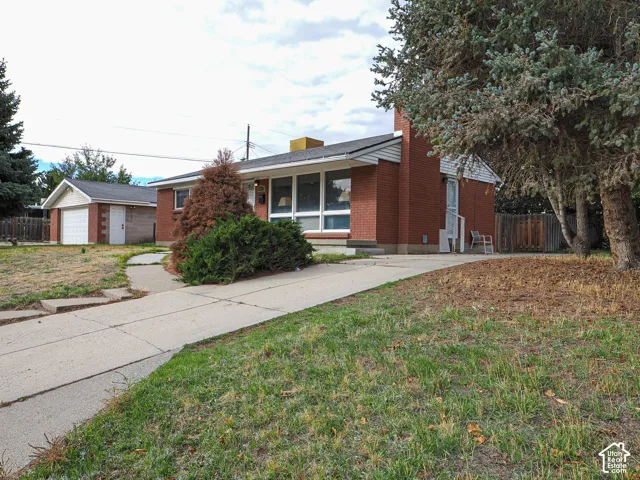 Single-story brick exterior residence featuring a chimney, a paved concrete driveway, a detached garage, and large multi-pane windows