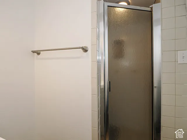 Shower stall with a framed textured glass door, square ceramic wall tiling, and a wall-mounted metal towel bar