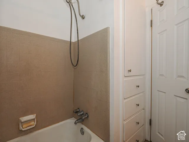 Built-in white cabinetry featuring multiple storage drawers and a cabinet door, accompanied by a bathtub with a tiled surround, wall-mounted handheld shower fixture, and a six-panel door