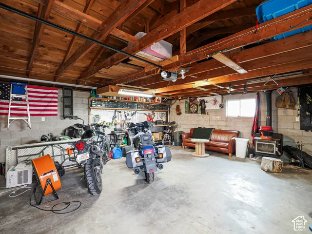 Attached garage featuring exposed timber ceiling joists, concrete block walls, a wood-burning stove, and fluorescent lighting