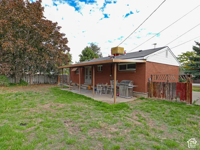 Red brick exterior featuring a covered concrete patio, gabled roofline, and wood-panel fencing