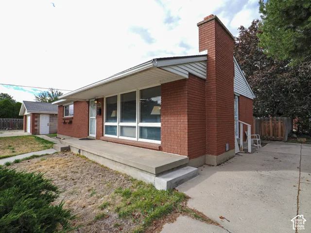 Red brick exterior featuring a prominent chimney, concrete front porch, large multi-pane windows, and a detached garage