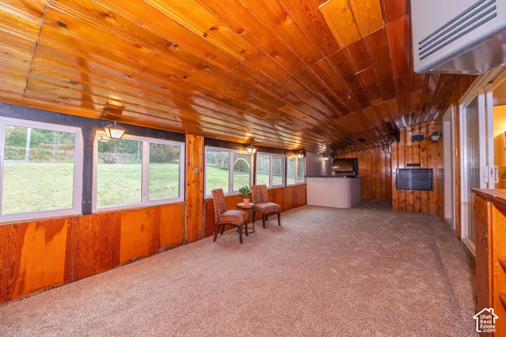 Enclosed sunroom featuring natural wood-paneled walls and ceiling, carpeted flooring, large multi-pane windows, and a built-in wet bar with a countertop