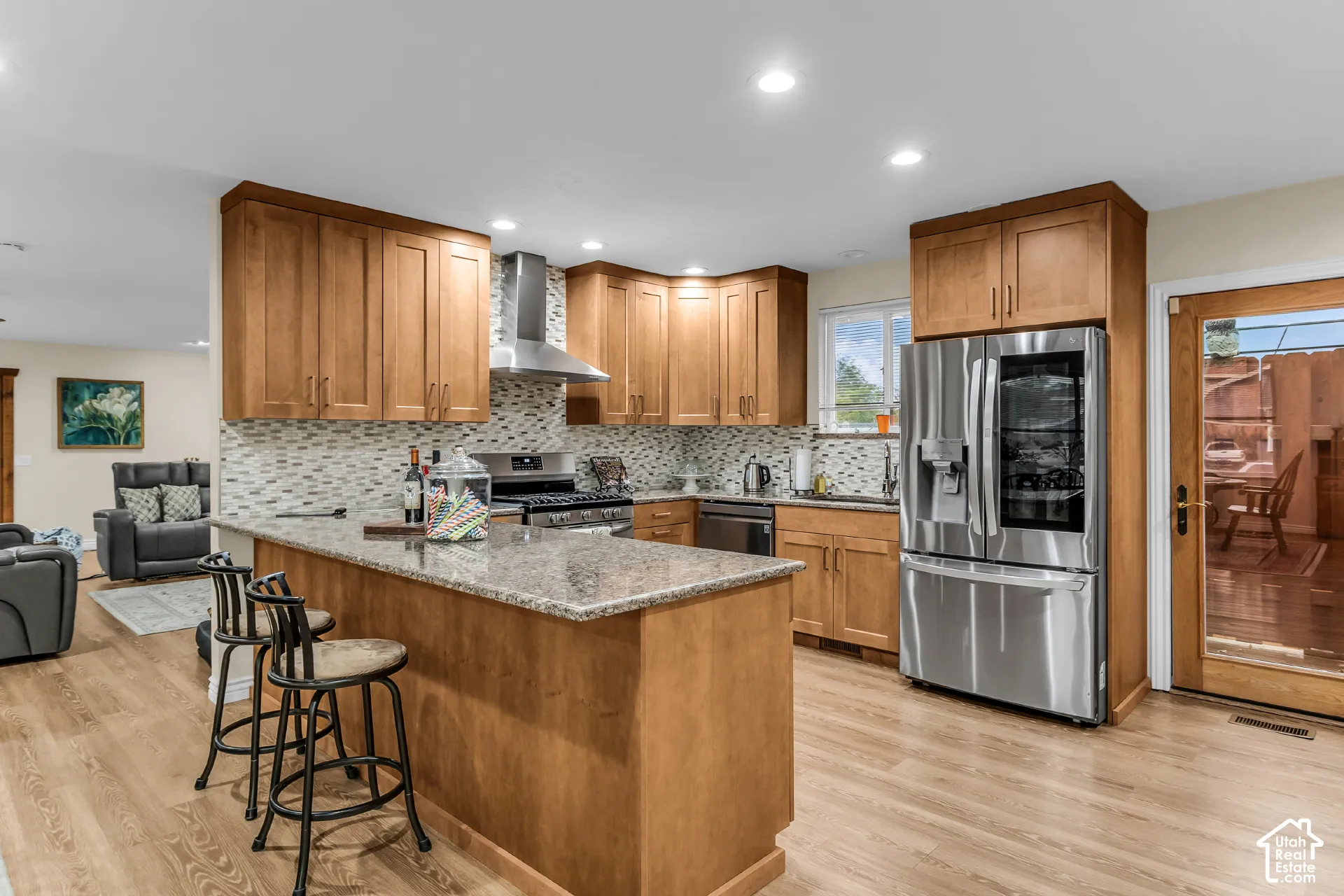 Kitchen featuring wooden cabinetry, stone-surface countertops, stainless steel appliances, a mosaic tile backsplash, and wood-finish flooring