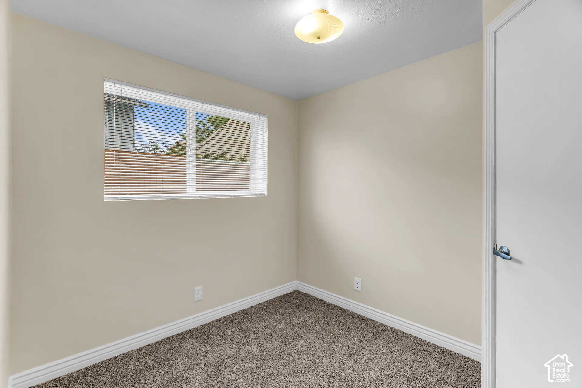 Interior space featuring neutral wall paint, textured carpeting, a horizontal sliding window with integrated blinds, and a semi-flush mount ceiling light fixture