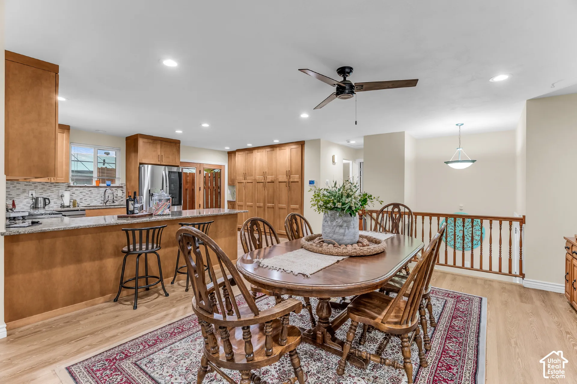 Open-concept interior featuring wood-finish flooring, recessed lighting, wood cabinetry, a stone-surfaced kitchen island, and a wooden stair railing