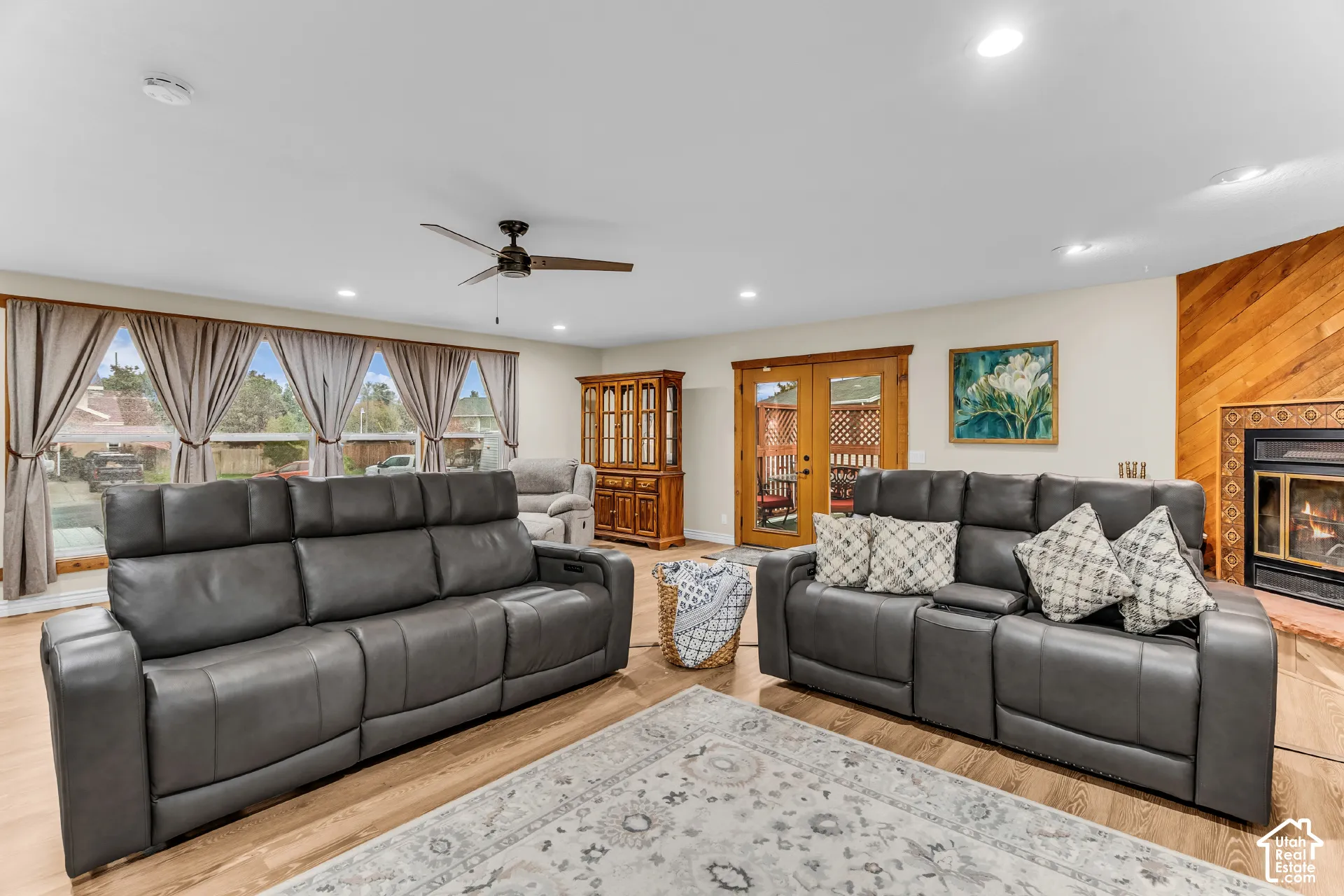 Living area featuring wood-finish flooring, recessed lighting, ceiling fan, fireplace with diagonal wood accent wall, and wood-framed glass exterior doors