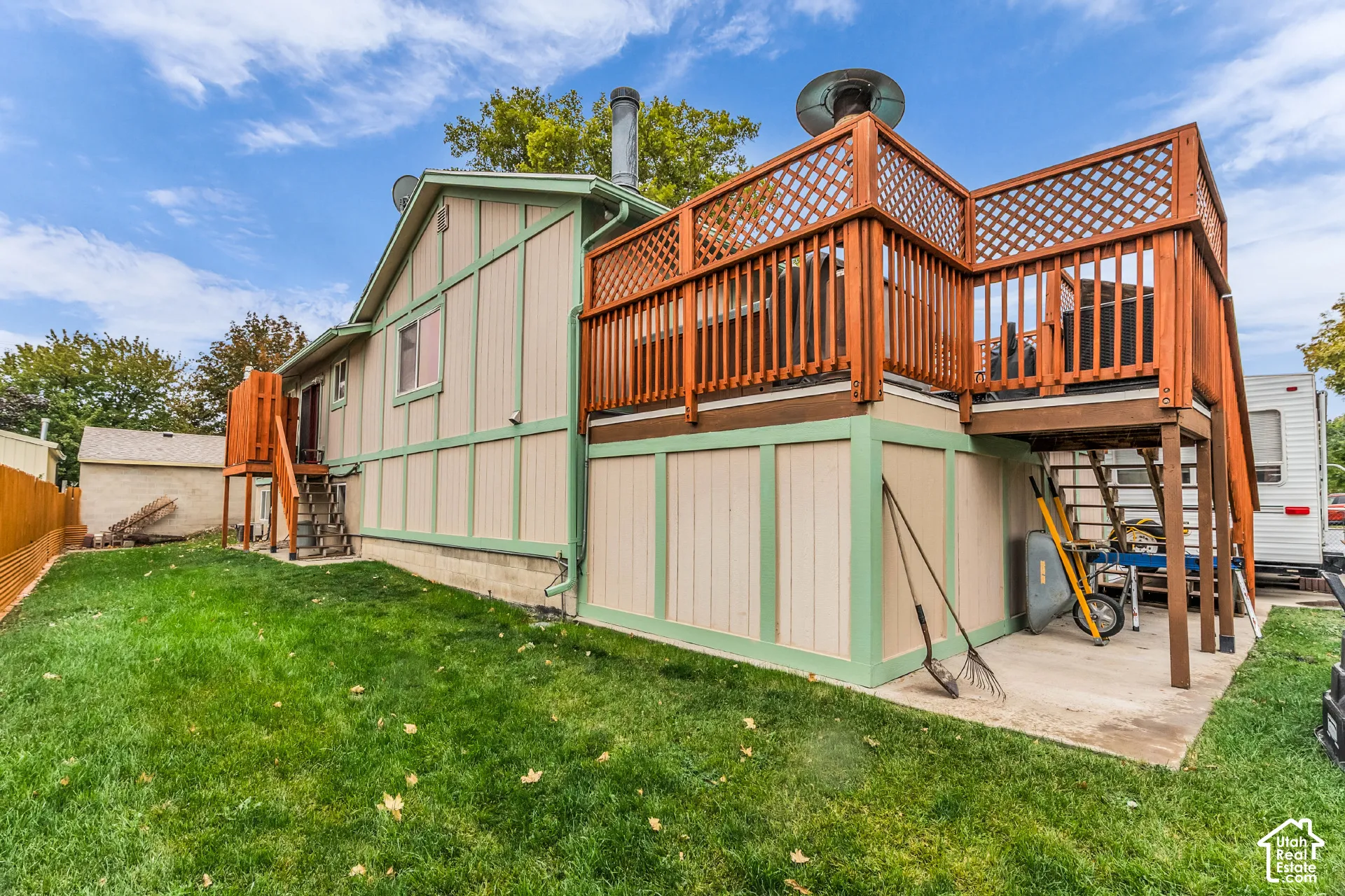 Exterior featuring vertical siding with decorative trim, an elevated wooden deck with lattice railing, a lower-level concrete patio, and a fenced yard