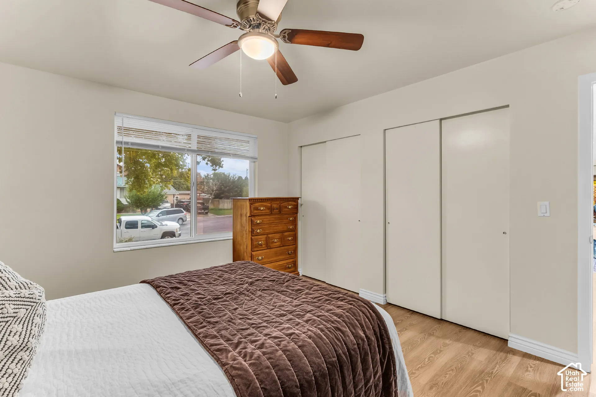 Room featuring wood-finish flooring, dual-panel closet doors, and a ceiling fan with integrated lighting
