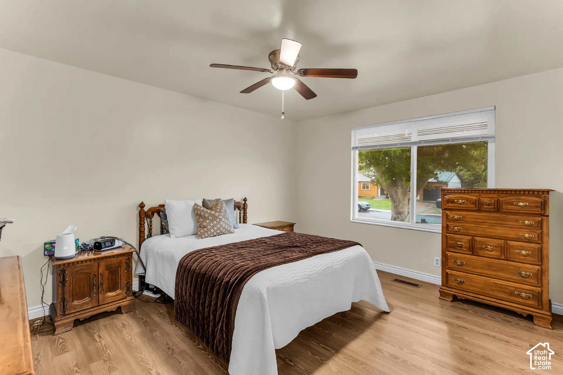 Room featuring wood-finish flooring, a neutral color palette, a large horizontal window, and a ceiling fan with integrated lighting