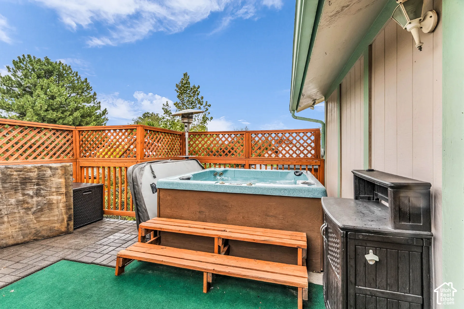 Outdoor deck featuring stone paver flooring, wood lattice privacy fencing, and an integrated spa