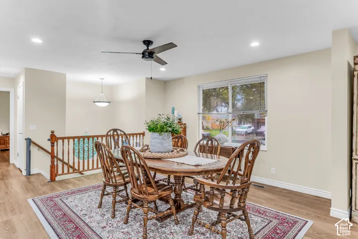 Wood-finish flooring, recessed lighting, ceiling fan with light kit, pendant lighting, and wooden staircase railing