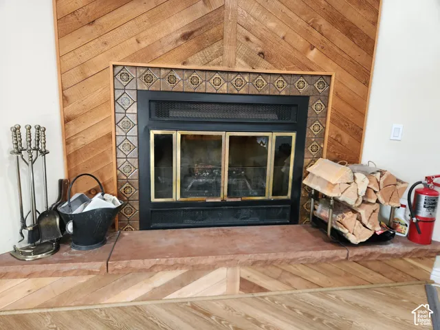 Fireplace featuring a decorative patterned tile surround, a brass-framed glass enclosure, and a natural stone hearth set against a wood-paneled accent wall in a chevron pattern
