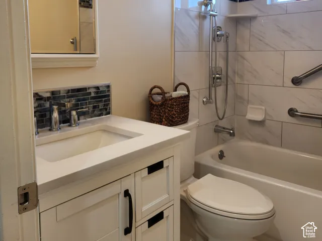 Bathroom featuring a white vanity with drawers, a rectangular undermount sink, a shower-tub combination with horizontal wall tiling, and decorative mosaic tile accents