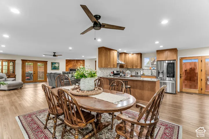 Open-concept floor plan featuring wood-finish flooring, a kitchen island with stone-style countertops, shaker-style cabinetry, recessed lighting, and dual sets of French doors