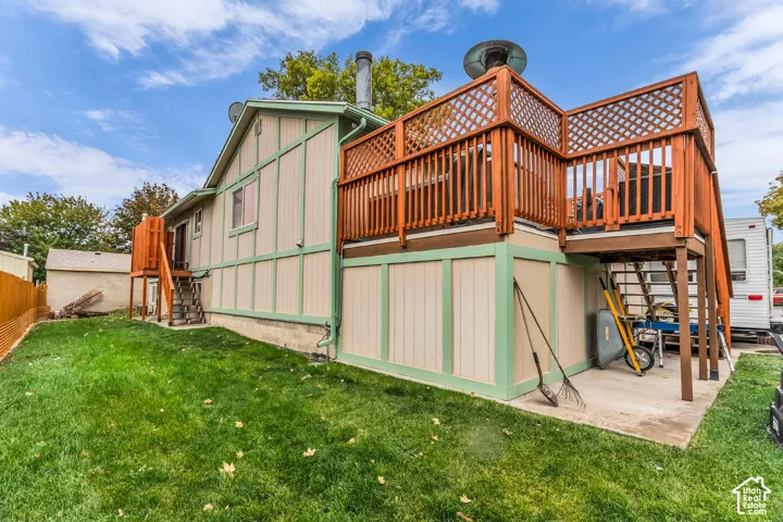 Exterior featuring vertical siding with decorative trim, an elevated wooden deck with lattice railing, a lower-level concrete patio, and a fenced yard
