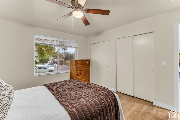 Room featuring wood-finish flooring, dual-panel closet doors, and a ceiling fan with integrated lighting