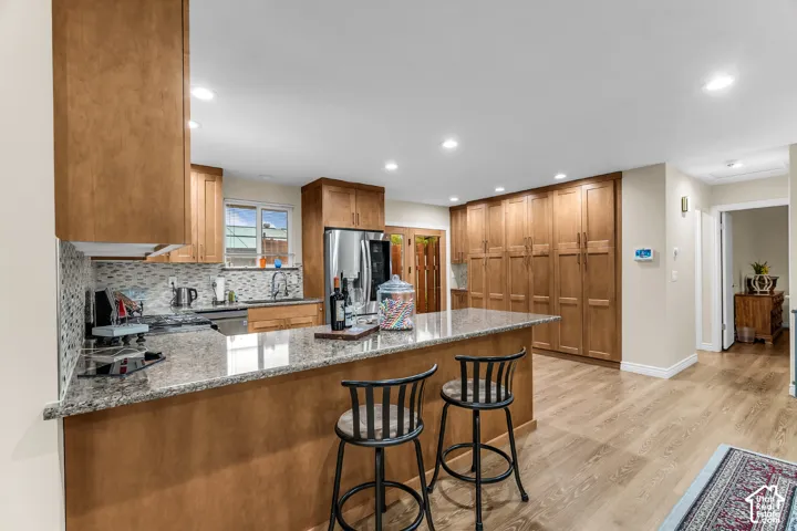 Kitchen featuring wood cabinetry, stone countertops, integrated cabinetry wall storage, recessed lighting, and wood-finish flooring