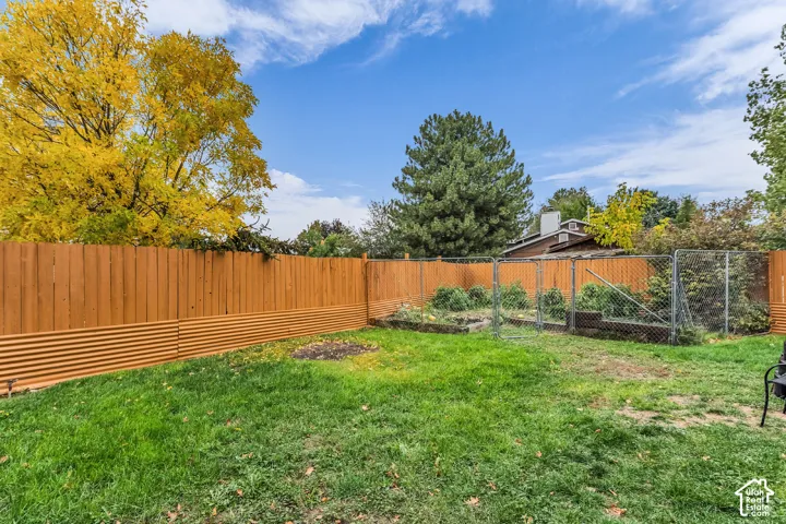 Backyard featuring a wood-panel fence with a corrugated metal base, a chain-link gate, a lawn area, and a brick-bordered planting bed