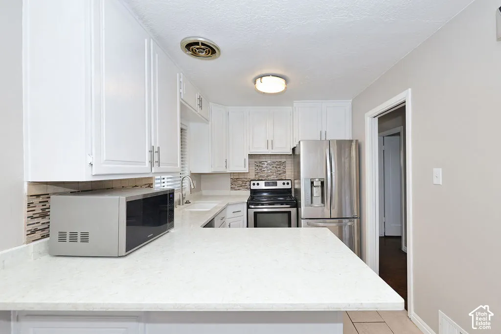 Kitchen featuring white cabinetry, solid-surface countertops, mosaic tile backsplash, stainless steel appliances, and ceiling lighting