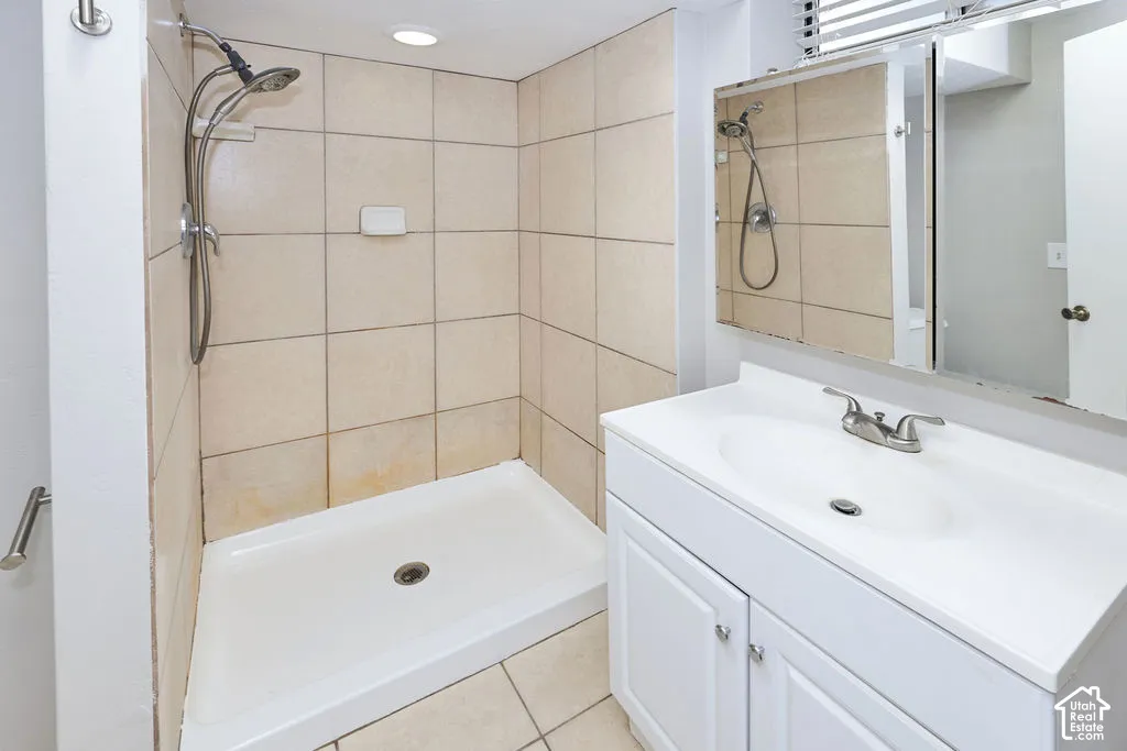 Bathroom featuring a walk-in shower with tile surround, white vanity cabinet, integrated sink, and mirrored medicine cabinet