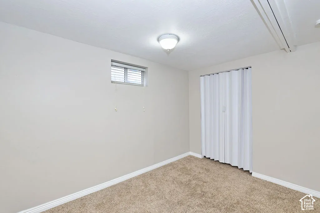 Neutral-toned room featuring neutral carpeting, a built-in accordion-style closet door, and an exterior window with a horizontal blind