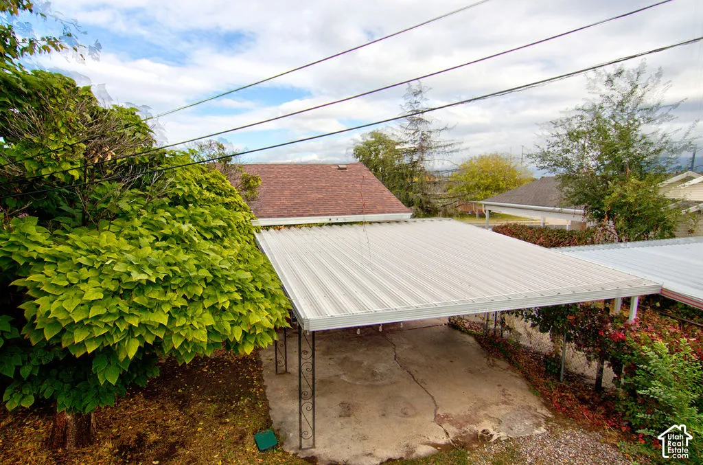 Covered carport featuring a metal roof, decorative wrought iron supports, and a concrete pad