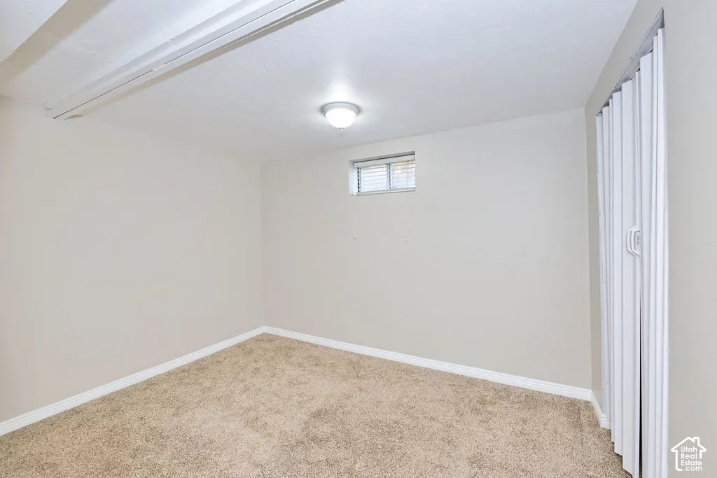 Neutral-toned interior space featuring wall-to-wall carpeting, a horizontal casement window, a central flush-mount ceiling light, and vertical folding door hardware
