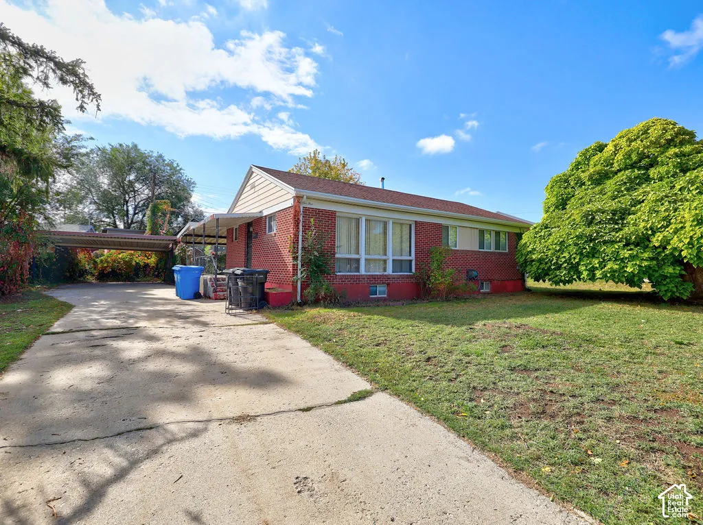 Red brick exterior featuring a shingle roof, large picture windows, a concrete driveway, and an attached carport