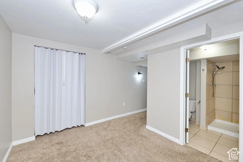 Carpeted room featuring a white accordion-style closet door, ceiling-mounted light fixture, and an entry to a tiled bathroom with a walk-in shower