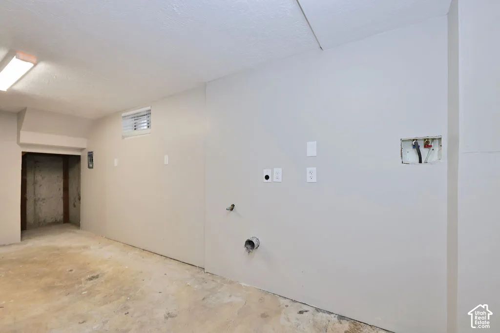 Utility area featuring concrete flooring, surface-mounted linear lighting, a recessed wall niche, and exposed plumbing hookups