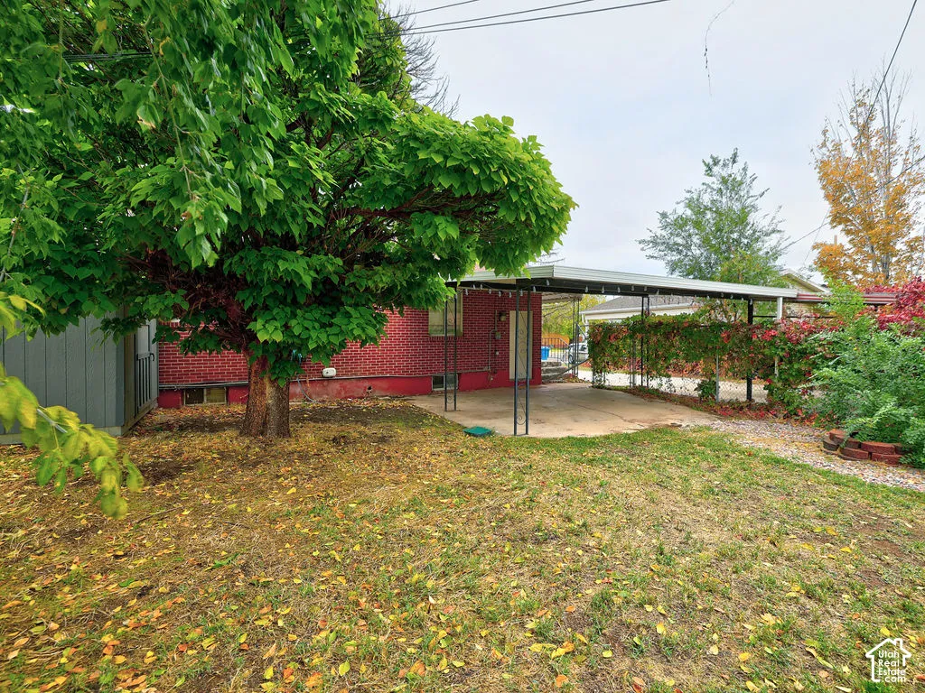 Exterior featuring red brick masonry, a covered concrete carport, and mature trees on a level lot