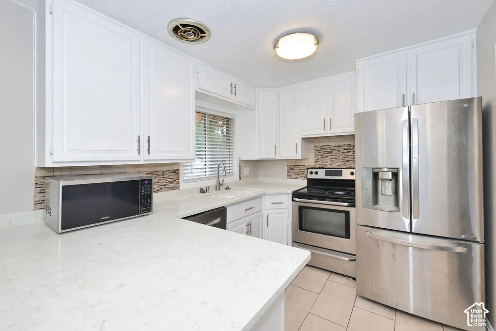 White cabinetry featuring modern hardware, solid-surface countertops, tile backsplash, stainless steel appliances, and a double-basin sink