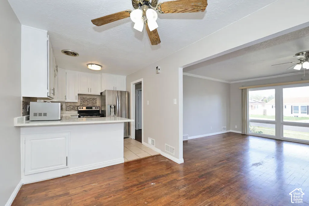 Wood-finish flooring, white cabinetry, a peninsula breakfast bar, built-in stainless steel appliances, and large windows providing natural light