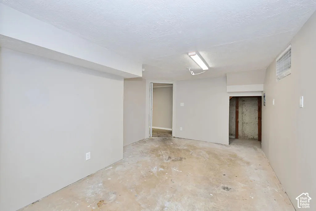 Neutral interior space with smooth-finish walls, a linear surface-mounted light fixture, and an unfinished concrete floor