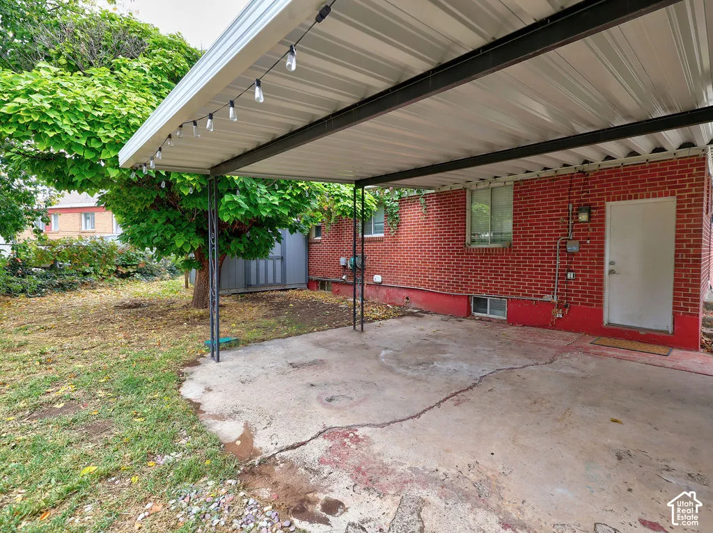 Red brick exterior featuring a metal-roofed carport and a concrete parking pad